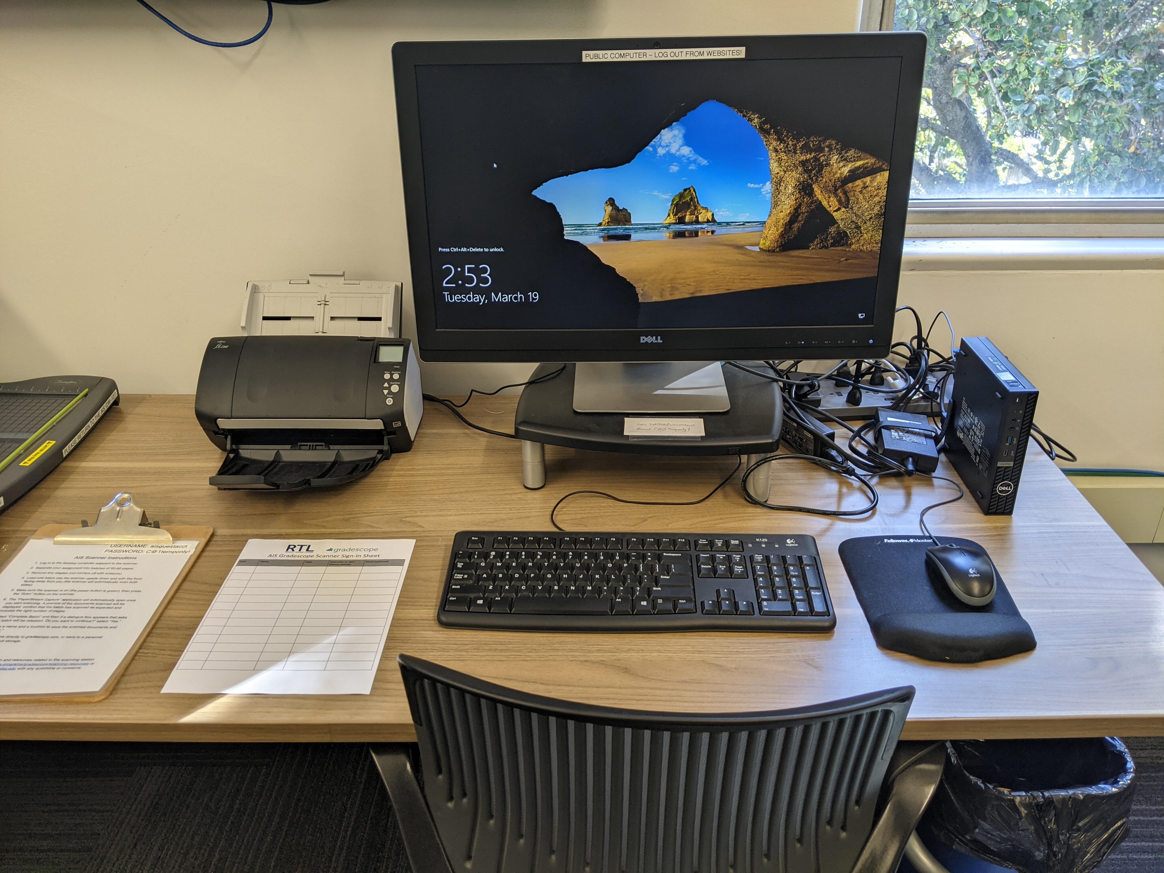 The document scanning station in the Academic Innovation Studio consisting of a desktop computer, keyboard, mouse, document scanner, and sign-in sheet on a desk with a desk chair.